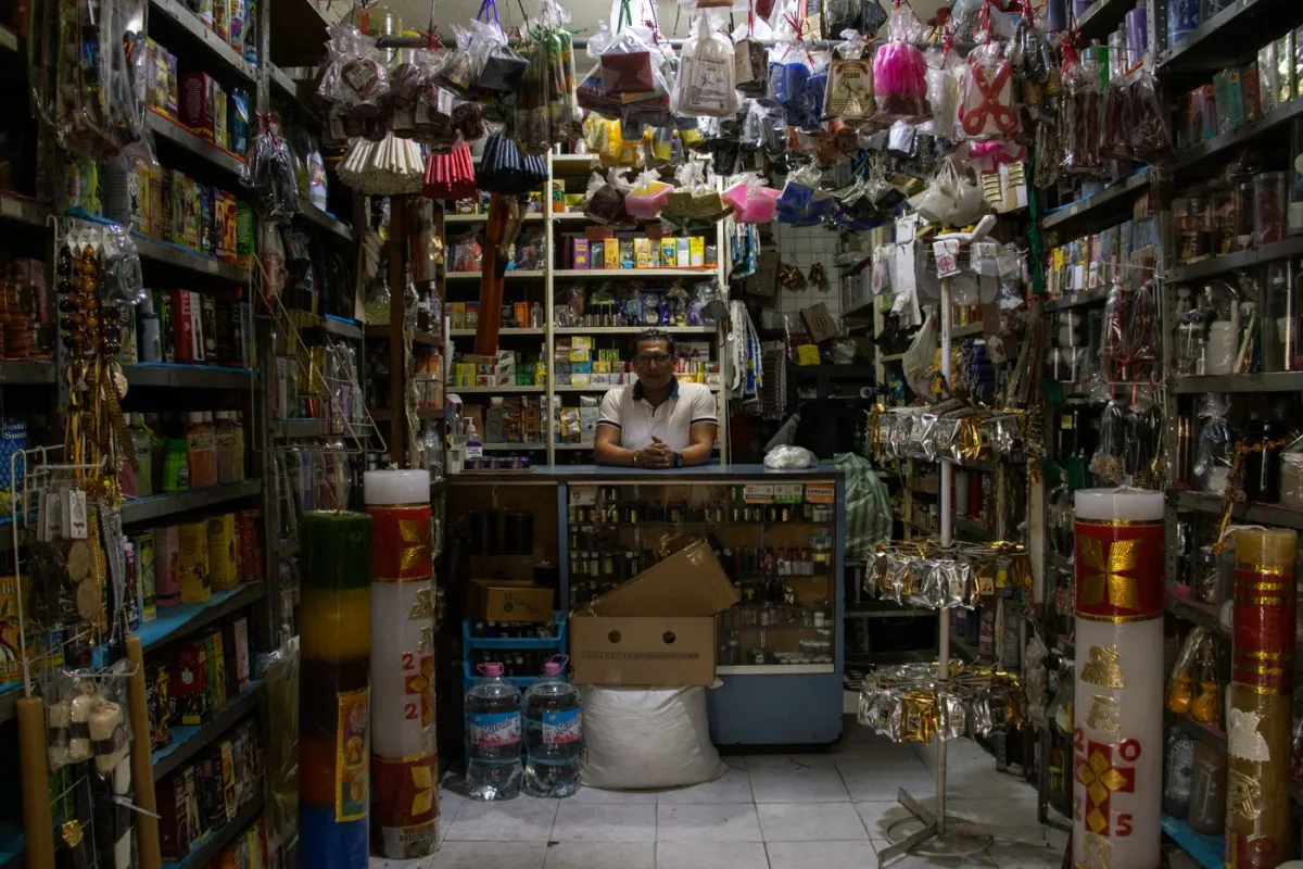 Shopkeeper behind the counter of a small shop stocked with everyday products